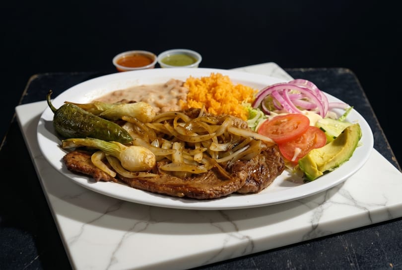 Carne asada with grilled onions, rice, beans, avocado, tomatoes, cucumber, and a jalapeño.