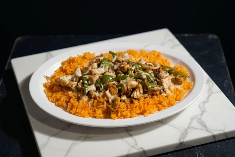 A white oval plate filled with orange rice, topped with chicken, green peppers, and a creamy sauce.