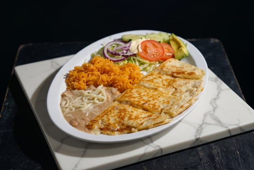 A plate of quesadillas, rice, beans, and a side salad with avocado, tomato, and onion.