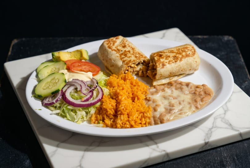 A burrito cut in half, served with orange rice, refried beans, and a side salad.